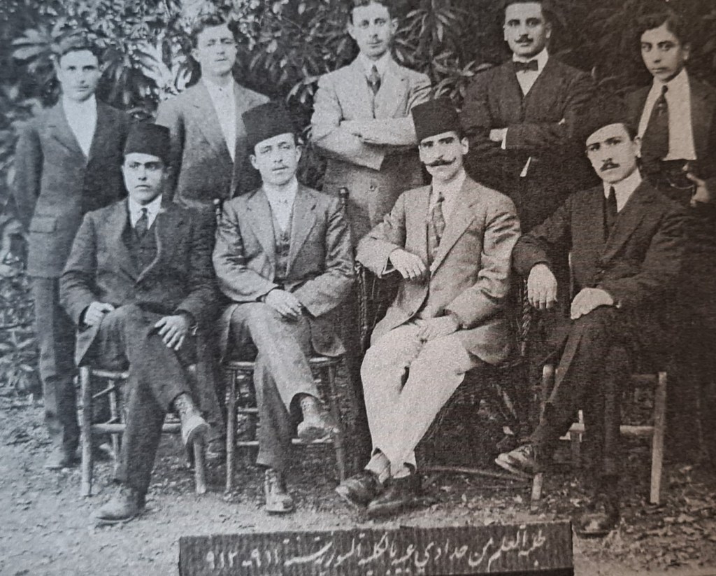 Black and white photograph of nine male students, four seated in the front and five standing at the back.